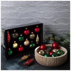 an assortment of christmas ornaments in a wooden bowl next to a black box with red and green baubles