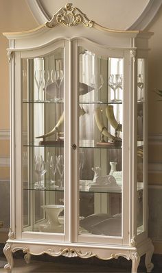 a white china cabinet with glass doors and gold trimmings on the top shelf