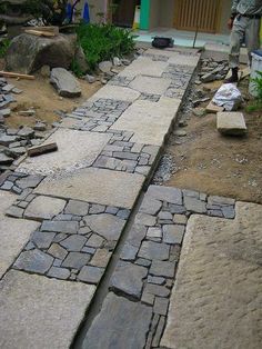 a man standing next to a stone path in the middle of a yard with rocks on it