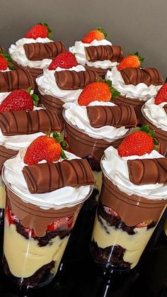 several desserts are arranged in rows on a black table with strawberries and whipped cream