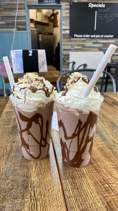 two cups filled with ice cream and chocolate on top of a wooden table at a cafe