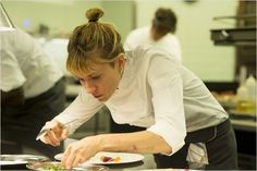 a woman in white shirt preparing food on top of a plate with utensils