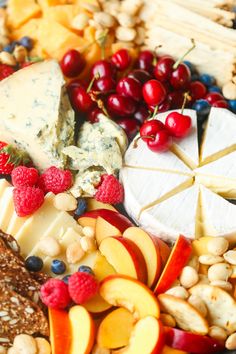 an assortment of cheeses, fruits and crackers on a platter with nuts