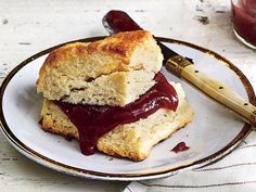 two biscuits with jam on them sit on a plate next to a jar of jelly