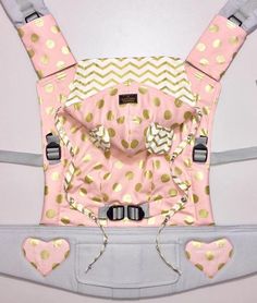 a baby carrier with pink and gold polka dots on it's front, attached to the back