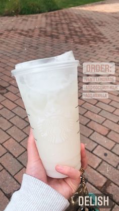 a person holding up a starbucks cup on the side of a brick road with words above it