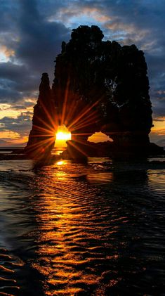 the sun is setting behind some rocks in the water