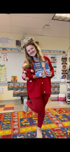 a girl in red is holding two books and smiling at the camera while standing on a rug