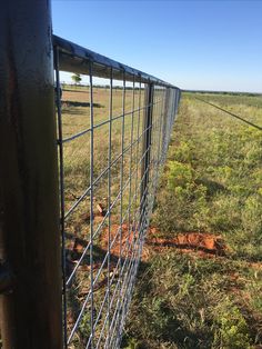 a fence that is in the middle of a field with grass and dirt on it