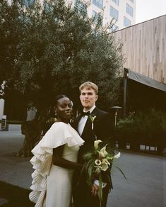 a man and woman standing next to each other in front of a building with trees