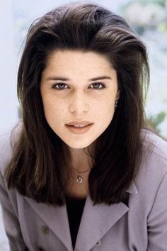 a woman with long dark hair wearing a gray jacket