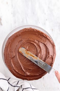 a knife is being used to spread chocolate frosting on a cake