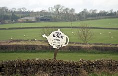 a tea room sign sitting on the side of a stone wall in front of a field