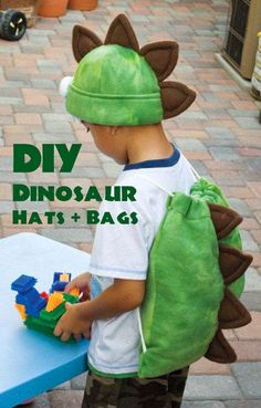 a young boy wearing a dinosaur hat and carrying a green bag with legos on it