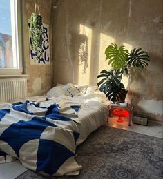 an unmade bed with blue and white comforter next to a potted plant