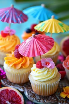 cupcakes decorated with colorful icing and umbrellas on a plate next to grapefruits