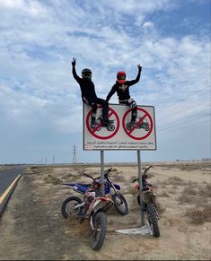 two motorcyclists are standing on a sign that says no motorcycles allowed in this area