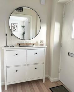 a white dresser with a round mirror on it's side and a door in the background