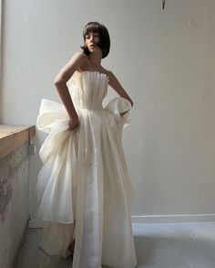 a woman in a white dress standing next to a window