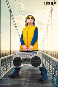 a man with headphones on holding a boombox in front of his face while standing on a bridge