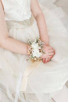 a woman wearing a white dress holding a bouquet of flowers in her hand and sitting on the floor