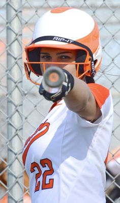 a woman in an orange and white uniform holding a baseball bat with her right hand