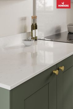 a white counter top sitting next to a sink in a kitchen with green cabinets and gold handles