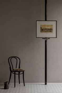 a chair sitting in front of a painting on the wall next to a table with a vase