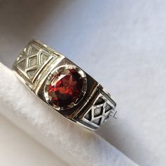 a silver ring with a red stone in the center on a white cloth covered surface