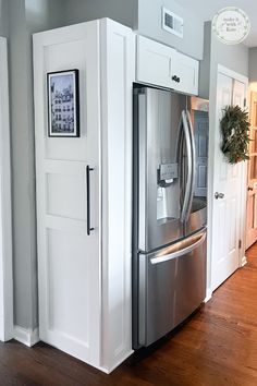 a stainless steel refrigerator and freezer combo in a kitchen with hardwood floors, white cabinets and gray walls