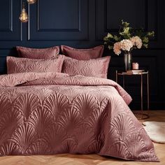 a bed with pink comforter and pillows in a dark colored room next to a table