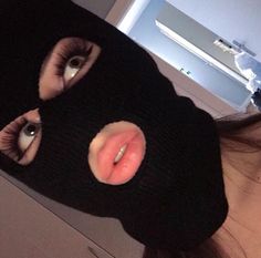 a woman wearing a black ski mask with her eyes open and tongue sticking out from under the hood