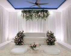 a living room decorated in white with flowers and greenery hanging from the ceiling above