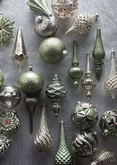 a collection of green and silver christmas ornaments on a table cloth with ribbons around them