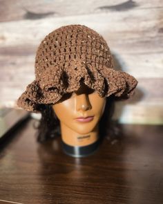 a mannequin head wearing a brown crocheted hat on top of a wooden table