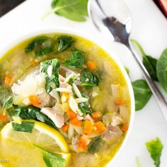 a bowl of soup with spinach, carrots, and other vegetables next to a spoon