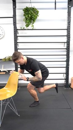 a man in black shirt and shorts doing squats on a chair with yellow seat