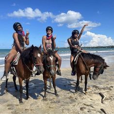 three girls riding horses on the beach with their arms in the air and one girl waving