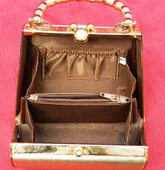 This is a small purse, 5 inches wide, 4 1/4 inches tall. It has a gold lame' fabric over a hard case with gold toned metal frame. It has a rigid handle, that stands 2 3/4 inches tall and 6 1/2 inches wide. The clasp is a flip cover type over a small pin. It has a clear glass jewel in top. the interior is a brown fabric with a small pouch on 1 side and a zipped pocket in middle. It is relatively clean with a small stain in 1 side, appears to be black ink and has been cleaned. The overall conditio Gold Rectangular Wallet For Evening, Compact Gold Wallet For Formal Occasions, Gold Rectangular Bag For Luncheon, Formal Gold Rectangular Coin Purse, Compact Gold Wallet For Everyday Use, Formal Compact Gold Wallet, Formal Gold Wallet With Gold-tone Hardware, Formal Gold Compact Wallet, Retro Gold Rectangular Evening Bag