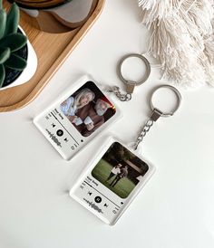 two keychains with pictures on them sitting next to a potted plant