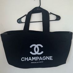 a black tote bag hanging from a hook on a wall with the word champagne printed on it