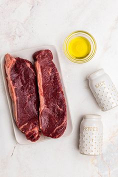 two raw steaks on a plate next to mustard and seasoning in small jars