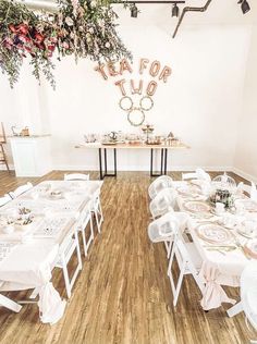 a room filled with tables and chairs covered in white tablecloths next to a floral centerpiece