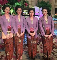 four women in purple outfits standing on a carpeted area with flowers and plants behind them