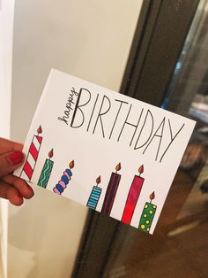 a person holding up a birthday card with candles on it in front of a door