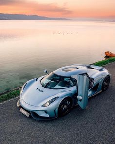 a silver sports car parked on the side of a road next to the ocean at sunset