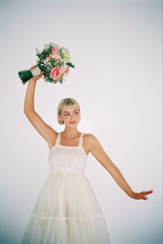 a woman in a white dress holding a bouquet of flowers up to her head with both hands