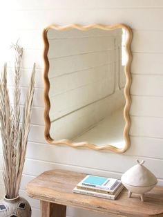 a mirror sitting on top of a wooden table next to a vase and potted plant