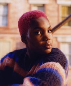 a woman with pink hair is looking off into the distance while standing in front of a brick building