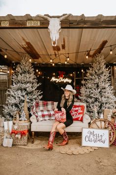 a woman is sitting on a couch in front of christmas trees and presents under a tent